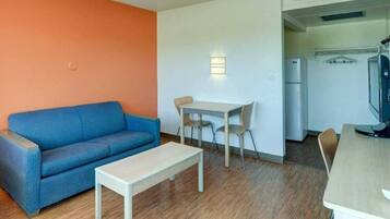 Un espacio habitable compacto con un sofá azul, una mesita, una zona de comedor con sillas y una kitchenette con refrigerador y televisor.