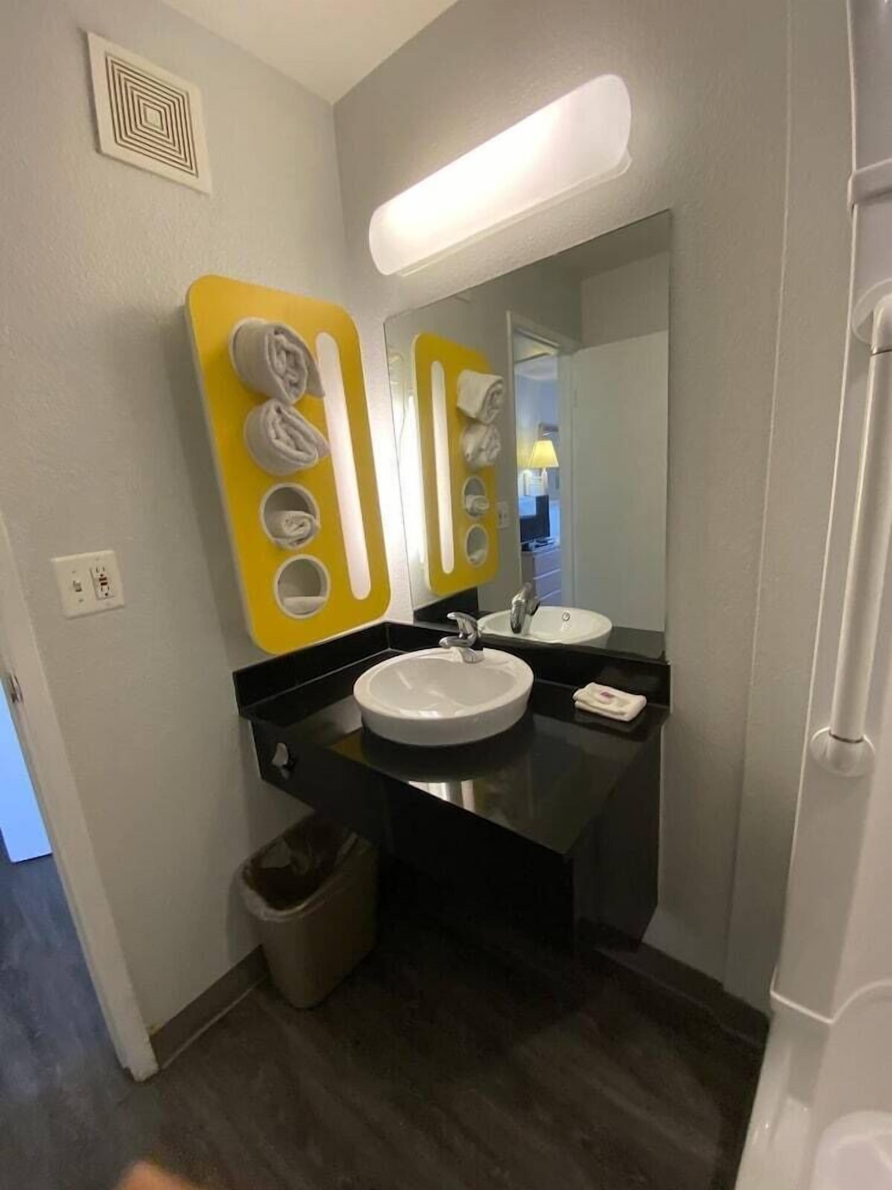 A modern bathroom with a black countertop, two sinks, a mirror, and a trash bin.