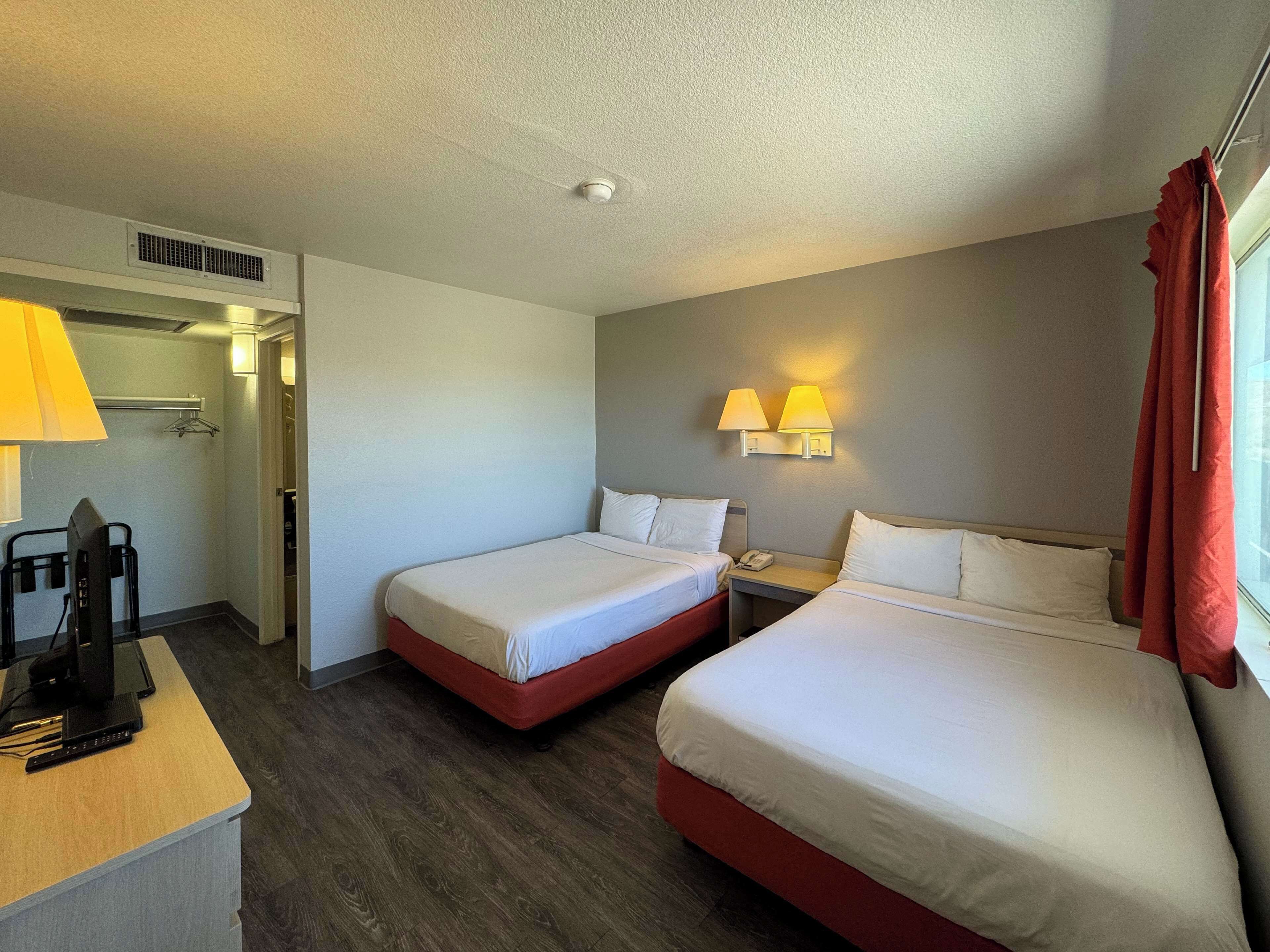 A hotel room with two beds, a desk with a computer, a telephone, and a wall-mounted lamp.