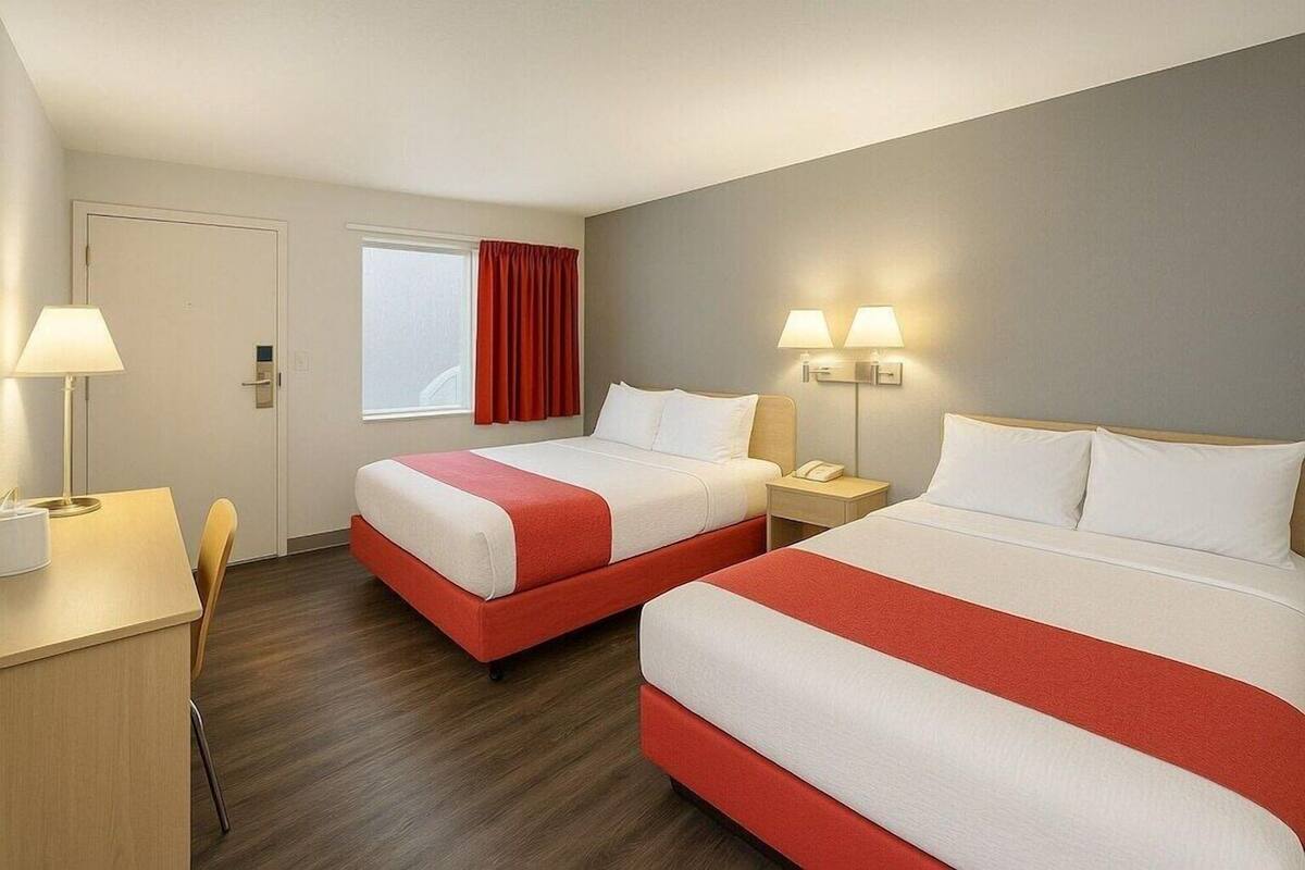 A hotel room with two beds, a desk, a chair, and a window with curtains.