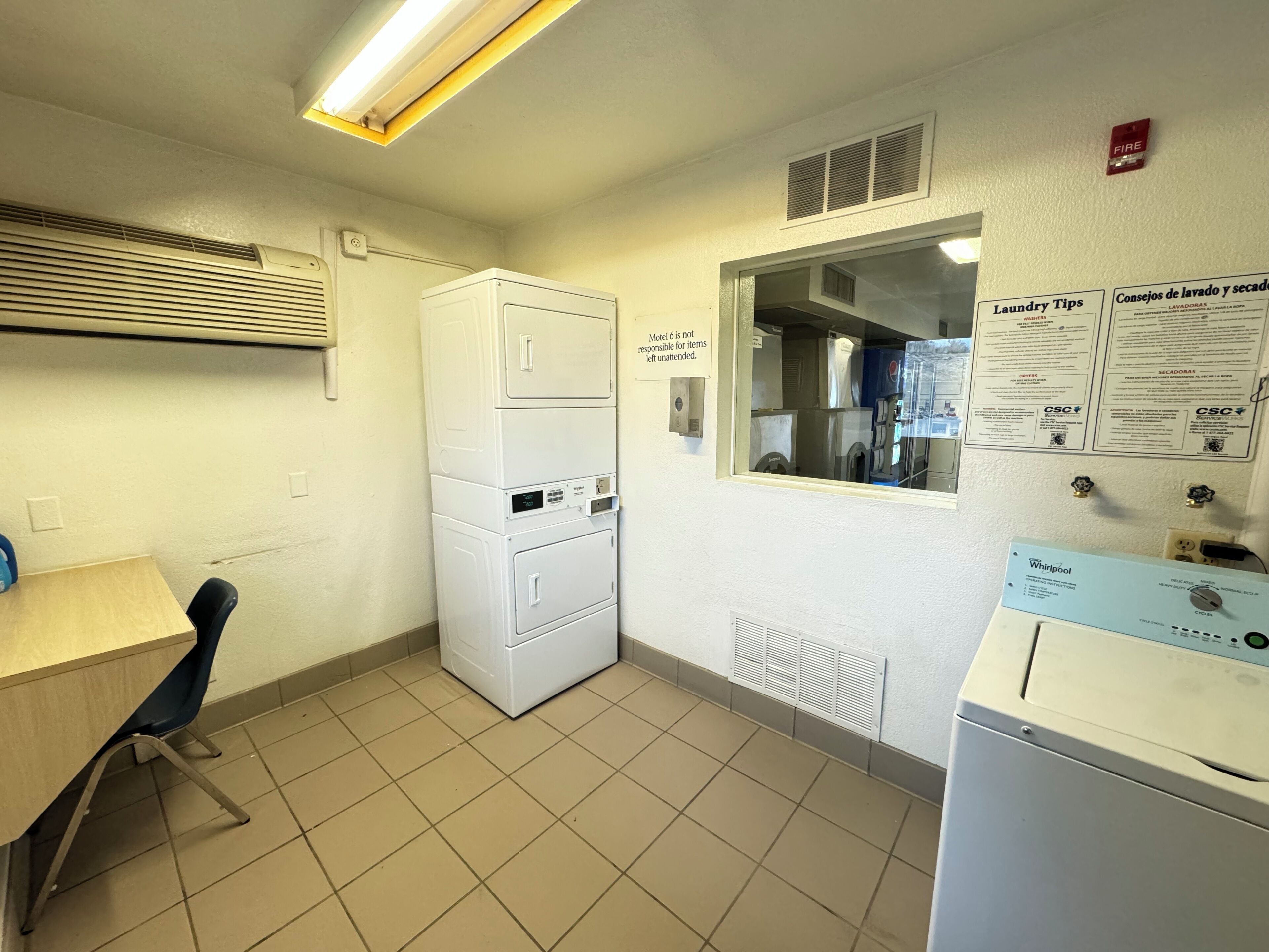 A laundry room with stacked washers and dryers, a table with a chair, and informational signs on laundry and cleaning.