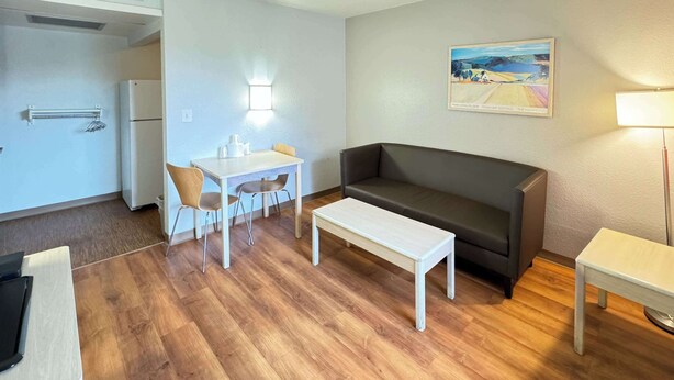 Un espace de vie compact comprenant un coin cuisine, un coin repas avec une table et des chaises, un canapé et un tableau accroché au mur.