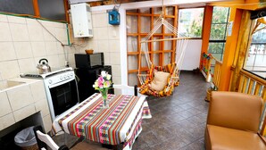 A kitchen with a gas stove, a microwave, and a sink. There is a dining table with a colorful tablecloth and a vase with flowers. A chair is placed at the table. - PRIVATE APART WITH A COZY TERRACE (Cusco)