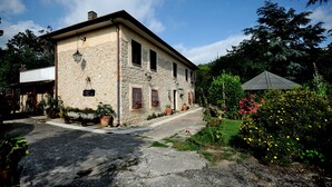 A stone building with a paved entrance, potted plants, and a garden with flowers. - ANCIENT FARMHOUSE SURROUNDED BY GREENERY (Sezze)