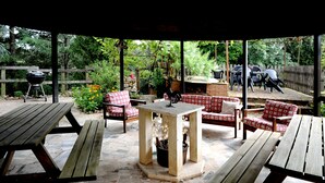 An outdoor patio with picnic tables, a barbecue grill, and a covered seating area with red and white checkered chairs. - ANCIENT FARMHOUSE SURROUNDED BY GREENERY (Sezze)
