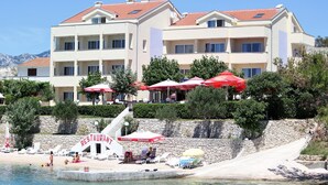 A hotel with multiple balconies, outdoor seating with umbrellas, and a beach area with lounge chairs. - Cozy apartment in Rtina with WiFi (Rtina)