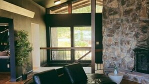Un salón amplio con chimenea de piedra, un sofá de cuero negro y un ventanal con vistas al exterior.
