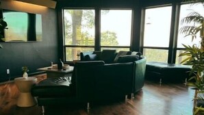 Una habitación amplia con un ventanal grande, un sofá oscuro y suelo de madera.