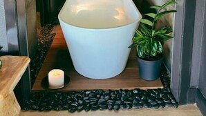 Un baño estrecho con paredes de madera, una bañera blanca grande, una vela pequeña y una planta en maceta.