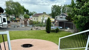 A wooden deck with a fire pit in the center, surrounded by a fenced yard with a grassy lawn and a few trees. - A Getaway Home~ Families & Big Groups  (Lewiston)