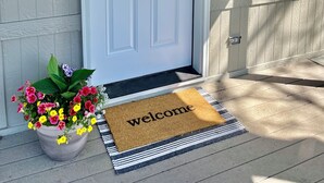 A white door with a glass panel, a mailbox, a welcome mat, and a potted plant with flowers. - A Getaway Home~ Families & Big Groups  (Lewiston)