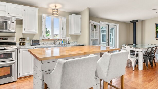 A modern kitchen with white cabinetry, a wooden island, and a dining area with white chairs. - A Getaway Home~ Families & Big Groups  (Lewiston)