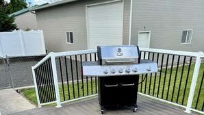 A barbecue grill on a wooden deck with a white fence and a house in the background. - A Getaway Home~ Families & Big Groups  (Lewiston)