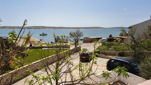 A coastal view with a stone pathway leading to a parked car, a boat in the water, and a clear sky. - Beautiful apartment in Kustici with WiFi (Kustici)