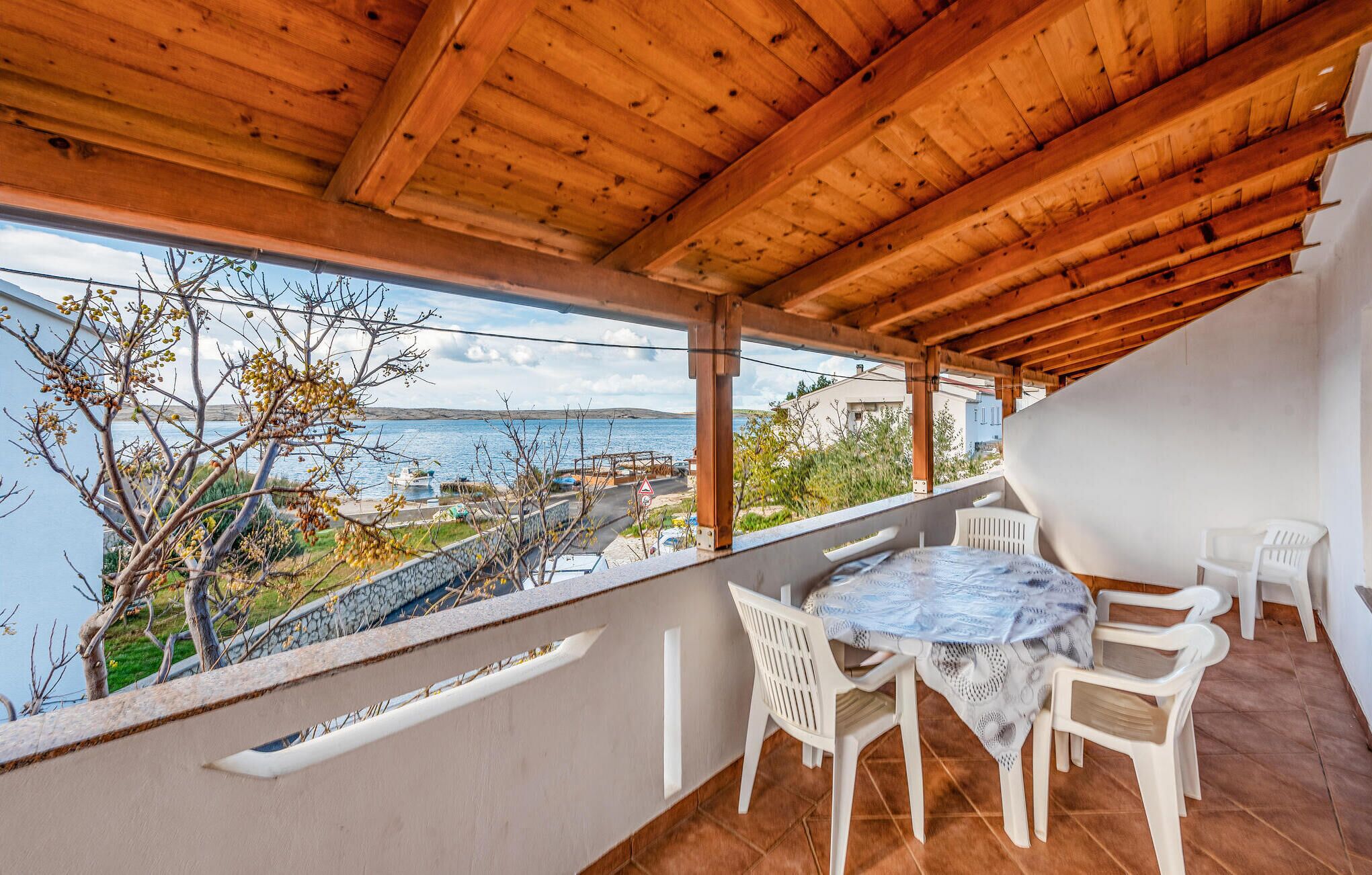Área externa coberta com mesa e cadeiras, com vista para um corpo d'água e uma paisagem montanhosa.