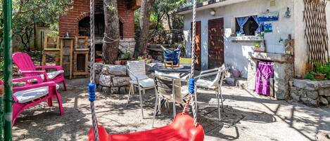 A rustic outdoor seating area with a swing, chairs, and a small table.