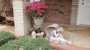 A brick building with a welcome sign, a potted pink flower, a wooden bench, and a stone angel statue.