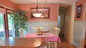A dining area with a wooden table and chairs, a red and white checkered tablecloth, and a hanging light fixture above.