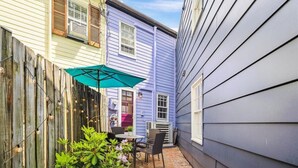 A narrow outdoor patio with a table and chairs, a green umbrella, and a wooden fence. - Historic Home with Parking Steps From Capital & USNA (Annapolis)