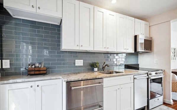 A modern kitchen with white cabinets, a stainless steel dishwasher, and a built-in oven.