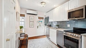 A modern kitchen with white cabinets, a stainless steel microwave, a black stove, and a tiled backsplash. - Historic Home with Parking Steps From Capital & USNA (Annapolis)