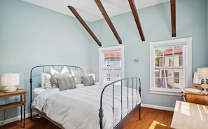 A bedroom with a bed, two windows, a nightstand, and a desk.