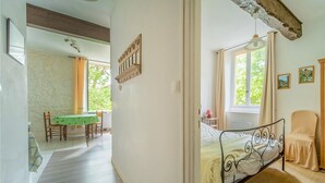 Ein Schlafzimmer mit einem Bett, einem Sessel, einem Tisch mit grüner Tischdecke und einem Fenster mit Vorhängen.