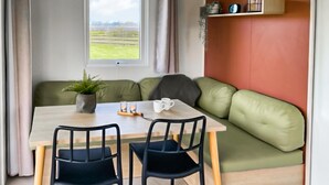 Una habitación acogedora con una mesa de comedor, dos sillas, un sofá verde, una planta en maceta y una ventana con vistas a un campo verde.