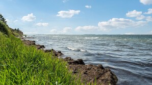 Paesaggio costiero con un litorale roccioso, zone erbose e cielo sereno.
