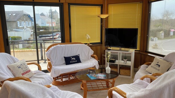 A sunlit room with wicker furniture, a television, and a view of the outside.