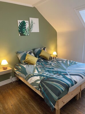 Une chambre à coucher avec un lit, deux lampes de chevet, un plancher en bois et deux œuvres d’art décoratives représentant des motifs de feuilles, accrochées au mur.