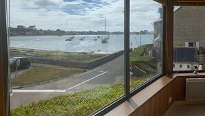 A view from a window overlooking a harbor with boats, a road, and a stone building.