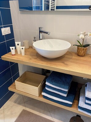 Une salle de bain avec un lavabo blanc, des serviettes bleues et un panier en osier contenant une orchidée.