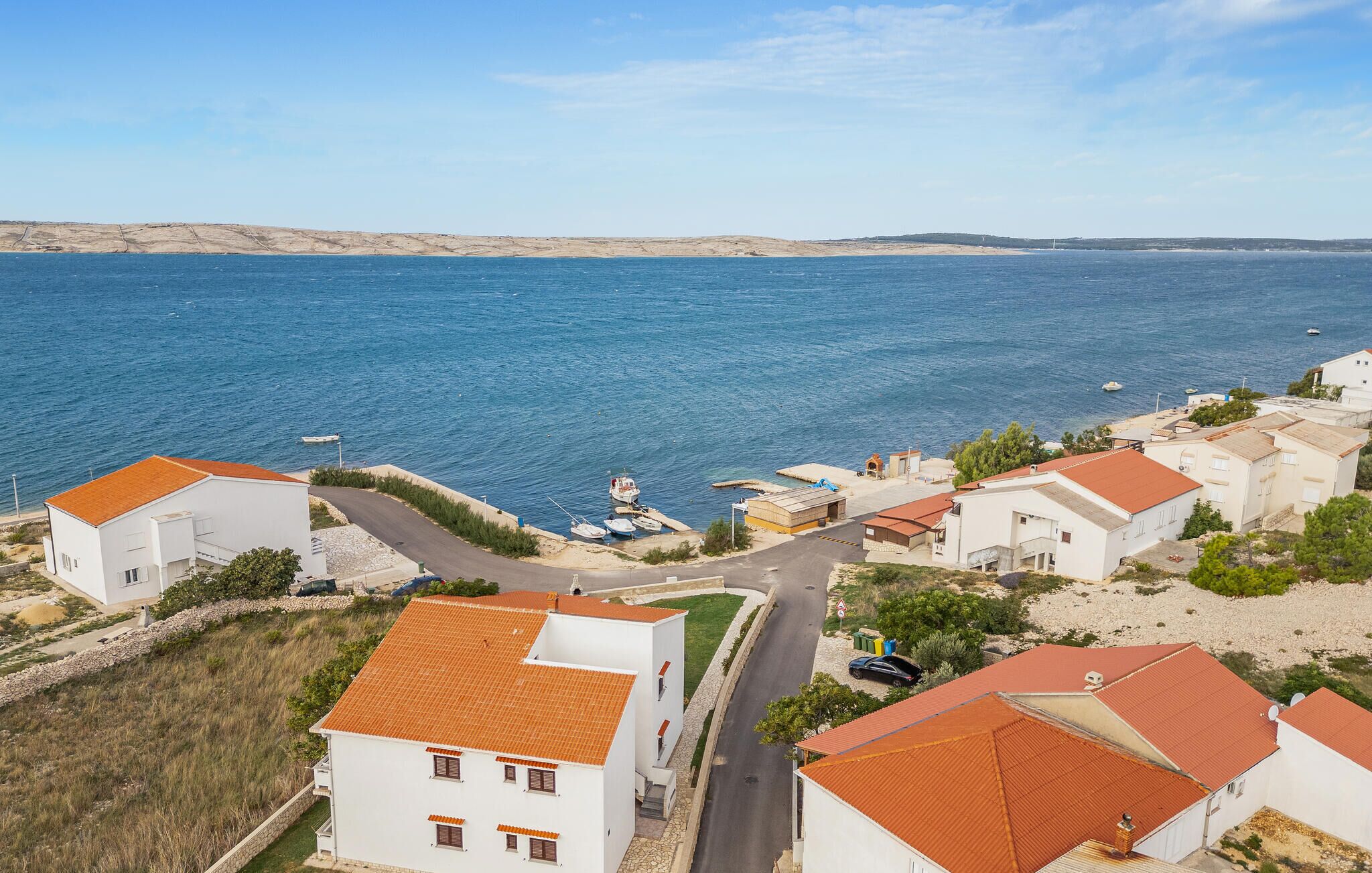 Ein Küstendorf mit weißen Gebäuden und roten Dächern, ein Yachthafen mit Booten und freie Sicht auf das Meer.
