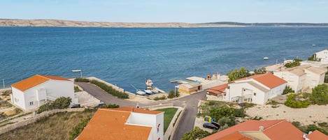 Un village côtier aux bâtiments blancs et aux toits rouges, un port de plaisance avec des bateaux, et une vue dégagée sur la mer.