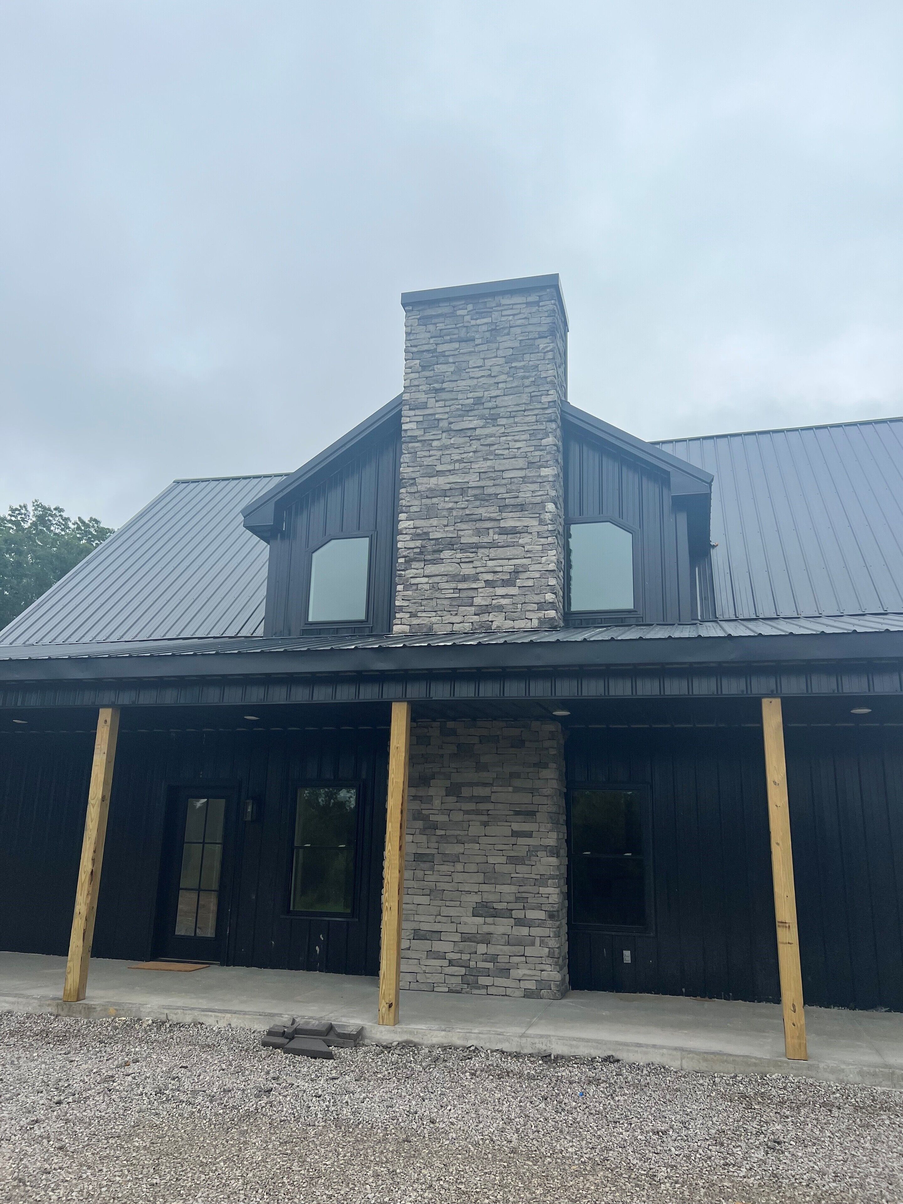 A building with a stone chimney, two large windows, and a metal roof.