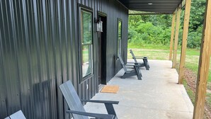 A covered outdoor seating area with metal walls and a concrete floor, featuring several lounge chairs and a wooden bench.