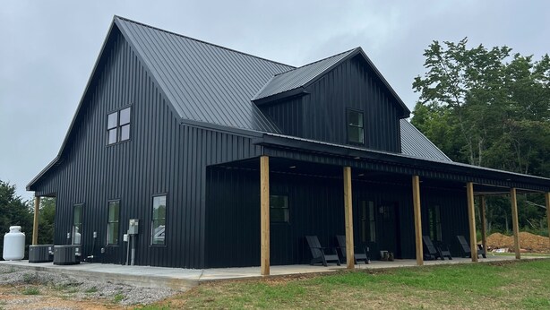 A modern black metal building with a large porch area and outdoor seating.