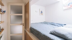 A bedroom with a bed, a door with frosted glass panels, a shelf with items, and a wall with a framed picture.