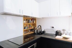 A modern kitchen with white cabinets, a black countertop, and a variety of kitchen appliances including a toaster and a kettle. - Beautiful, Sun-kissed Studio—Faubourg Saint-Martin (Paris)