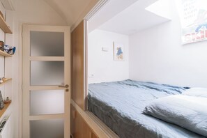 A bedroom with a bed, a wardrobe, and a door leading to another room. - Beautiful, Sun-kissed Studio—Faubourg Saint-Martin (Paris)