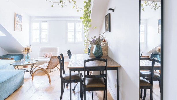 A bright, open-plan living space with a dining area, wooden flooring, and a large mirror.