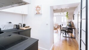 A modern kitchen with a black countertop, a kettle, and a toaster. There is a dining area with a table and chairs, and a hanging plant.