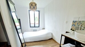 A room with a bed, a window, a hanging light fixture, and a tiled backsplash. - Maisonnette du Foirail, Proche Centre-ville Espalion. À 1 min des Berges du Lot! (Espalion)
