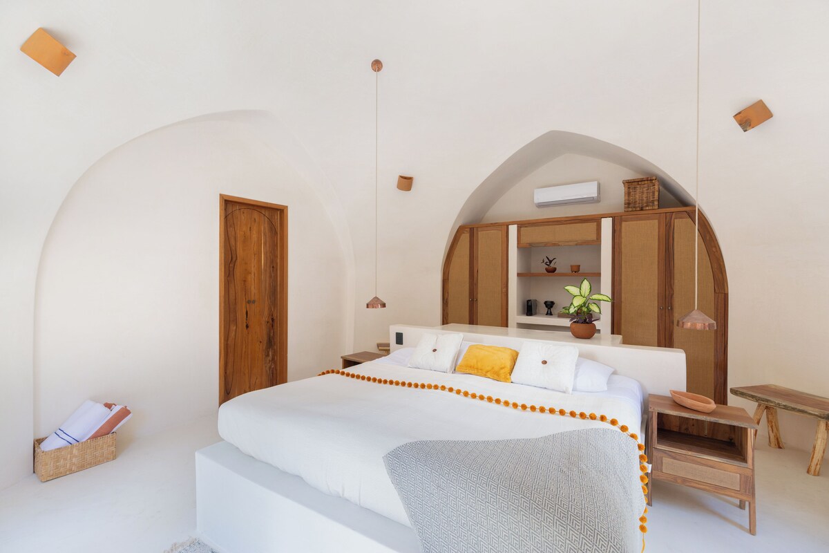 A bedroom with a large bed, wooden wardrobe, and a small table with a plant.