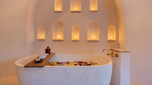 A spa room with a freestanding bathtub, a wooden tray with towels, and a wall-mounted candle holder with candles. - Villa Sanah (Tulum)