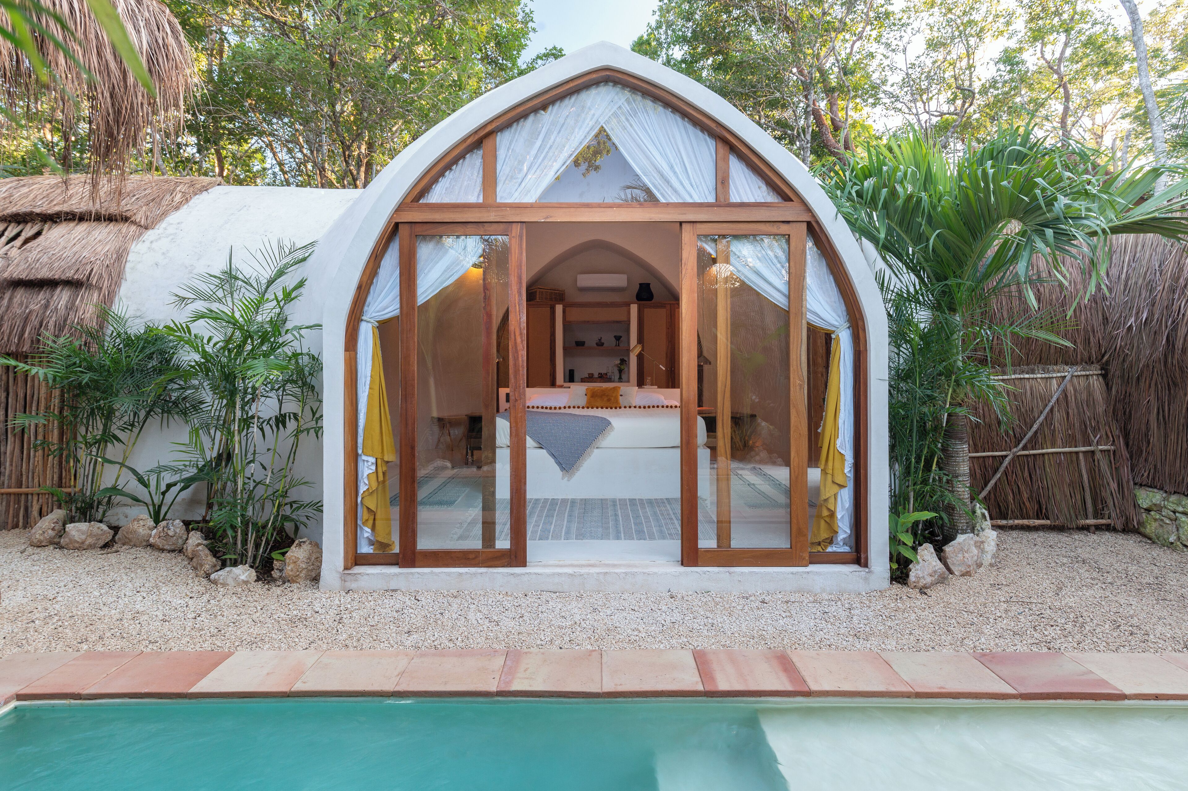 A dome-shaped structure with a glass door, a bed inside, and a pool in the foreground.