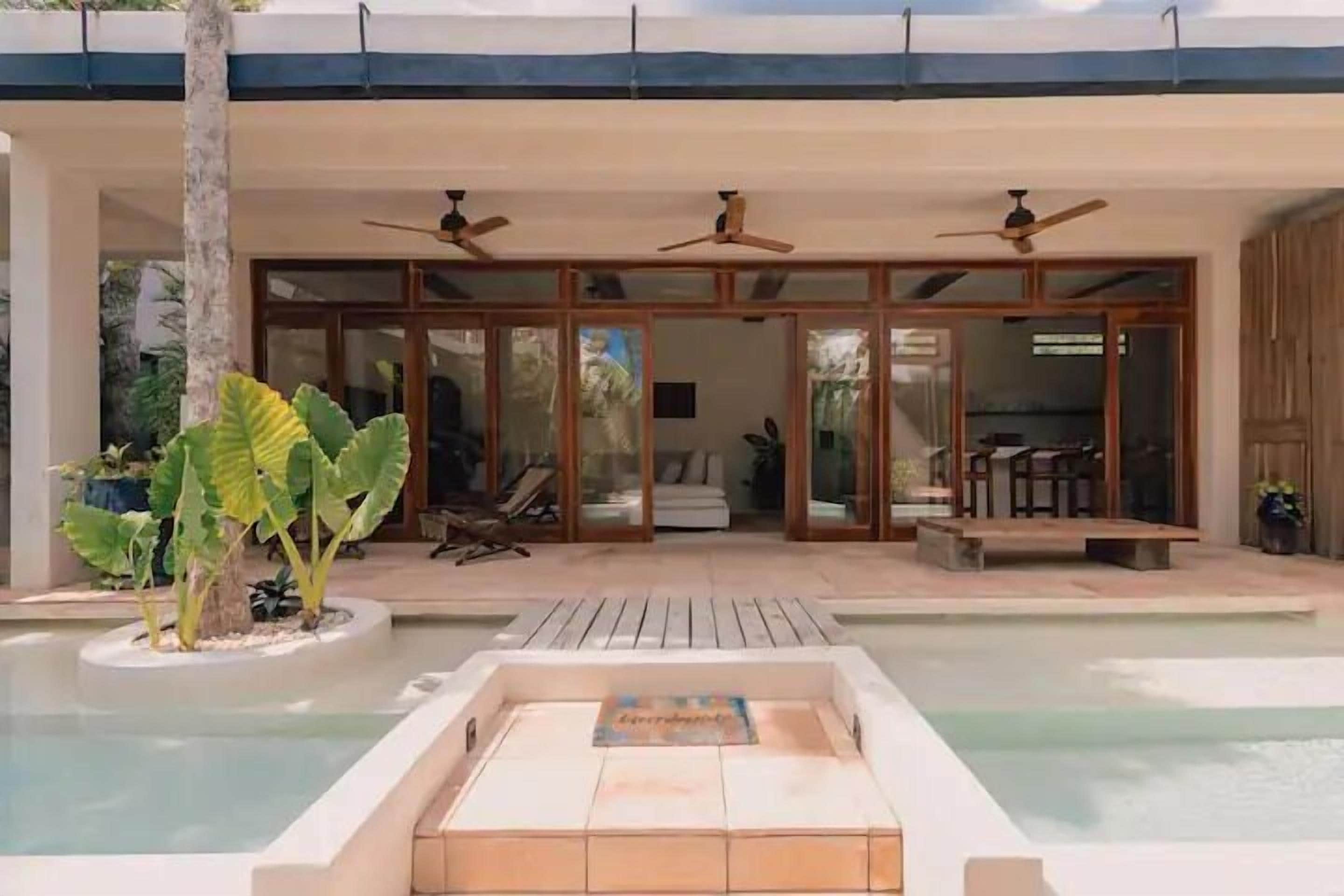Ein moderner Poolbereich im Freien mit Liegestuhl, Deckenventilatoren und einer Holzterrasse.