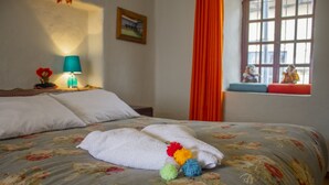 A neatly made bed with a floral bedspread, a white towel, and colorful pom-poms on it. - CENTRAL PLAZA APARTMENTS (Cusco)