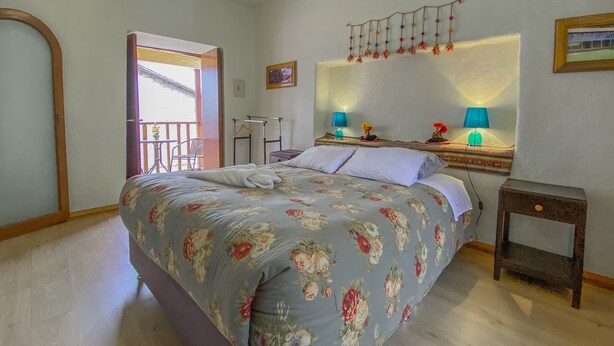 A bedroom with a bed, a nightstand, a mirror, and a window with a balcony. - CENTRAL PLAZA APARTMENTS (Cusco)